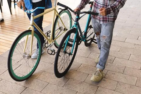 Mid section of two mixed race male friends wheeling bicycles in the street Stock Photos