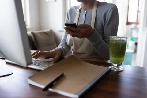 Mid section of woman in apron using computer and smartphone Fotos de archivo