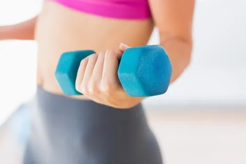 Mid section of a woman lifting dumbbell weight in gym Stock Photos