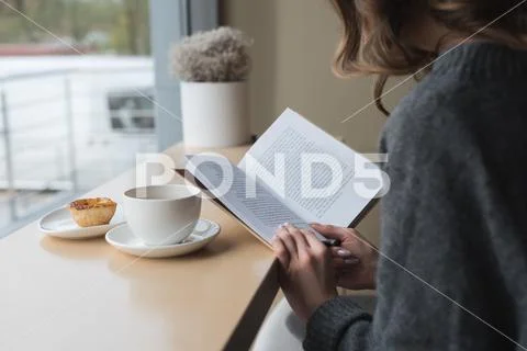 Mid Section Of Woman Reading Book At Cafe