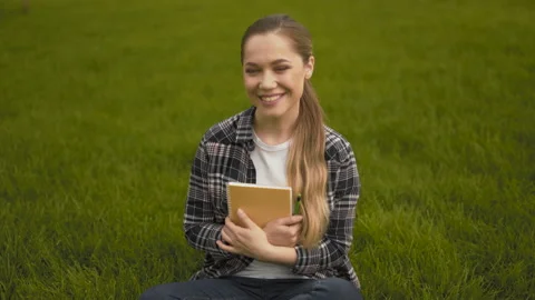 Mid shot. 20 years old girl in a plaid shirt sits on the grass and laughs Stock Footage 126036036