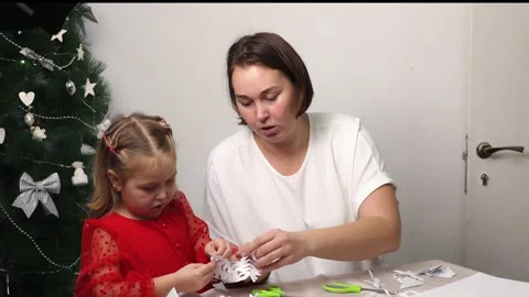 Mid shot of Caucasian mother and daughter are cutting snowflakes out of paper Stock Footage 321302425