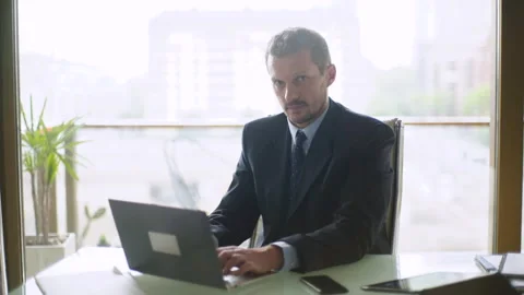 Mid-shot front view of male lawyer looking at camera while typing on laptop Video stock 277972073