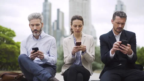 Mid-shot front view of three coworkers sitting next to each other on park bench Stock Footage 277975181