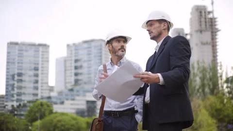 Mid-shot front view of two architects wearing hard hats looking at blueprints Stock Footage 277974387