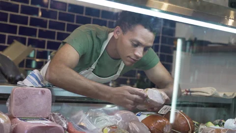 Mid-shot low angle view of young boutique gourmet shop owner choosing cold cuts Stock Footage 277963589