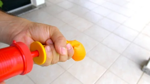 Mid shot of man inflating a orange balloon with a pump in slow motion Stock Footage 123243190