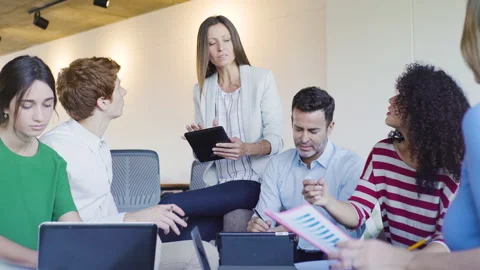Mid-shot side view of relaxed group of coworkers going over details of marketing Stock Footage 278026985