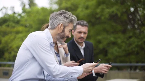 Mid-shot side view of three coworkers sharing work information on smartphones Stock Footage 277975011