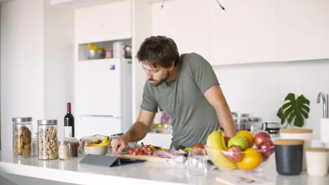 Mid-shot side view of young man chopping vegetables while following recipe Stock Footage 277968955