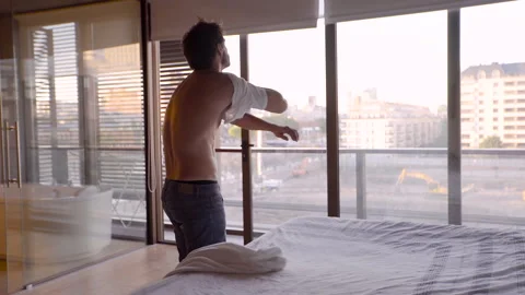 Mid-shot side view of young man with bare torso walking in to his bedroom and Stock Footage 277970184