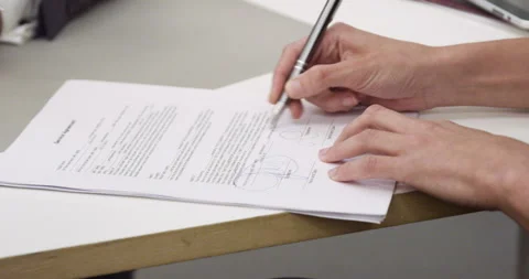 Mid-shot view of unidentified person's hands signing papers on top of desk Stock Footage 277950283