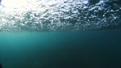 Midday sunlight sparkles through rippled ocean surface into deep teal water Vidéo 348702170