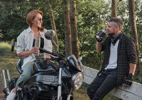 Middle age couple drinking tea, sitting on a motorcycle, traveling together on a Stock Photos