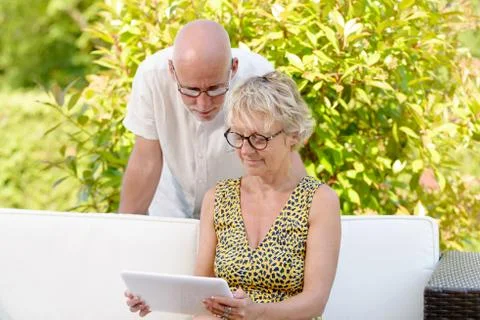 Middle age couple, smiling, using a tablet in their garden Stock Photos