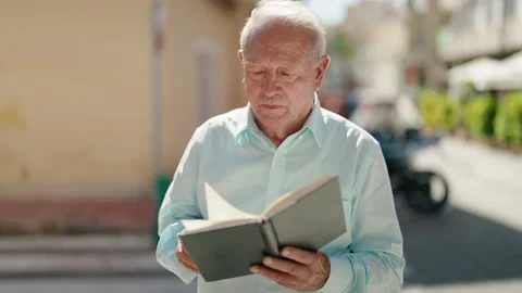 Middle age grey-haired man reading book at street Video stock 229561271