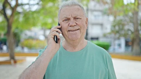 Middle age grey-haired man smiling confident talking on the smartphone at par Stock Footage 247385069