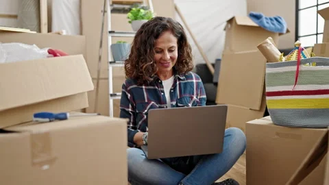 Middle age hispanic woman using laptop sitting on floor at new home Video stock 242346157