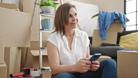 Middle age hispanic woman using smartphone sitting on floor at new home Stock-Footage 243499820