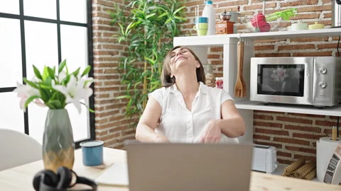 Middle age hispanic woman using laptop stretching arms at dinning room Video stock 243500071