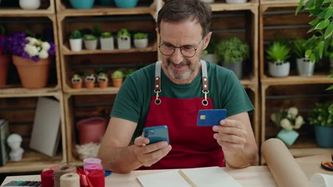 Middle age man florist using smartphone holding credit card at florist Stock Footage 205530352