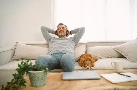 Middle age man sits on sofa listening to music for sleep with chihuahua dog 스톡 사진