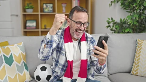 Middle age man supporting soccer team watching game on smartphone at home Stock Footage 246146794