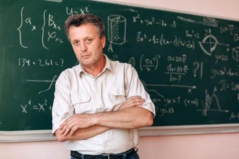 Middle age teacher  standing folded hands next  the blackboard looking at the Stock Photos