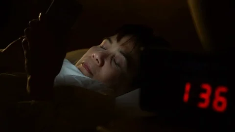 Middle age woman using a smartphone in her bed at night . Stockbeeldmateriaal 125171634