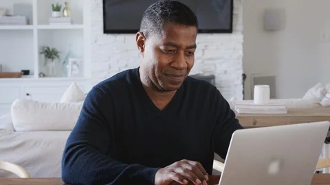 Middle aged African American man sitting at a table using laptop computer at Stock Footage
