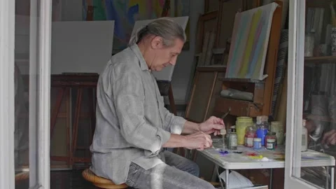 Middle aged artist with a ponytail preparing oil paints in his sunny studio Vídeos de archivo 147201405