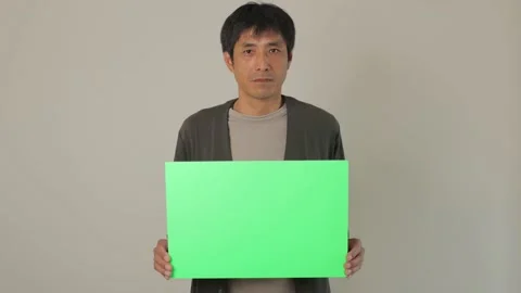 Middle aged asian man holding a green chroma board. Serious face. 25P. Stock Footage 224899643