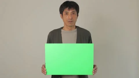 Middle aged asian man holding a green chroma board. Serious face. Stock Footage 224904006
