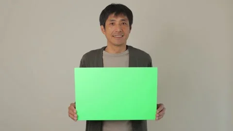 Middle aged asian man holding green board and smiles. For chromakey editing. Stock Footage 224904040