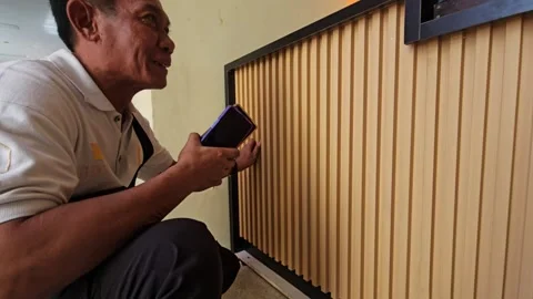 Middle Aged Asian Man Holding Smartphone Inspecting Wooden Slatted Wall Stock Footage 340001344