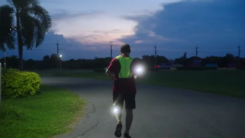 Middle-aged Asian man jogging safely at twilight with reflective gear Stock Footage 335759860