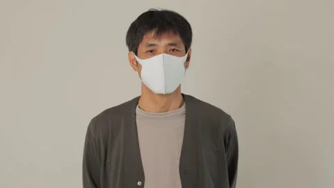 Middle aged asian man with mask on looks at the camera. Reluctant. 25P. Stock Footage 224899706
