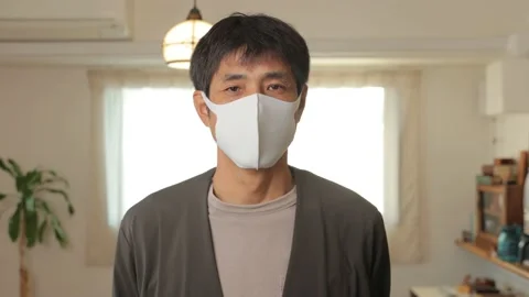 Middle aged asian man with mask on looks at the camera. Reluctant. 25P. Stock Footage 224900137