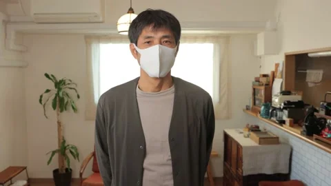 Middle aged asian man with mask on looks at the camera. Reluctant. 25P. Stock Footage 224900190