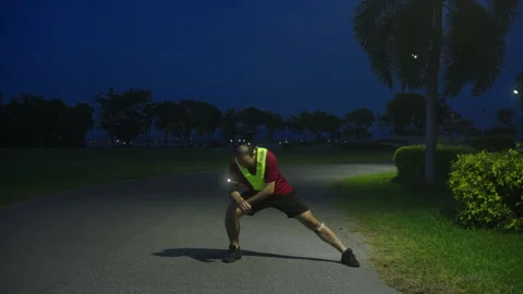 Middle-aged Asian man performing dynamic stretching before night jogging Stock Footage 335759858