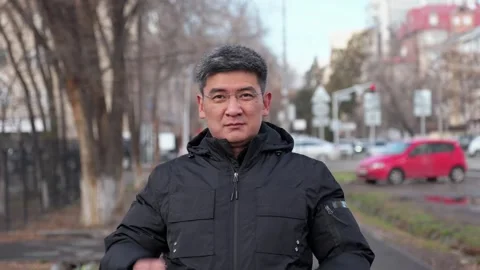 Middle aged asian man putting on eyeglasses outdoors in city street Stock Footage 323620634