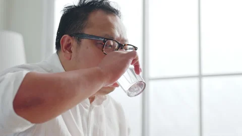 Middle-aged Asian man taking pill of medicine while sitting on sofa at home Stock Footage 232081017