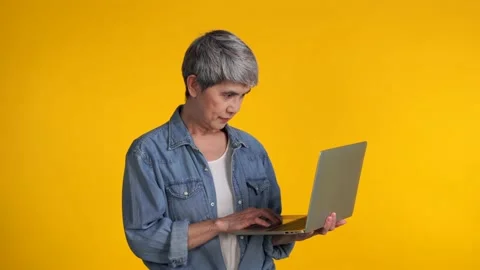 Middle aged Asian woman using laptop isolated on yellow background Stock Footage 159845652