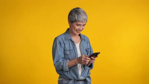 Middle aged Asian woman using smartphone isolated on yellow background Видео 159845700