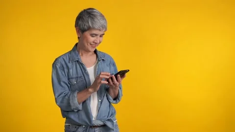 Middle aged Asian woman using smartphone isolated on yellow background Видео 159845715