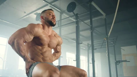 Middle-aged athlete sits in gym and tenses muscles on bare muscular torso Stock Footage 240248124