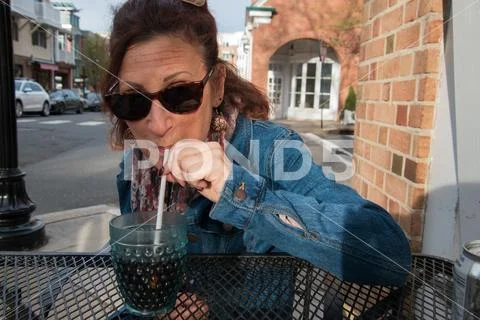Middle aged baby boomer woman sitting at an outdoor restaurant table by a str Stock Photos