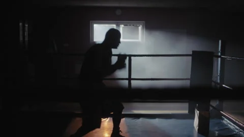 A middle aged bald boxer training in a dark gym with light coming from the .. Stock Footage 258245648