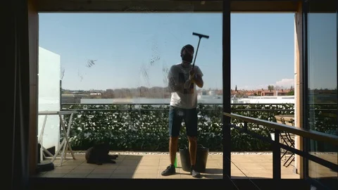 Middle-aged bearded man with his dog cleaning the windows of the terrace seen Stock Footage 127832474