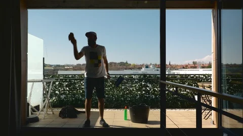 Middle-aged bearded man with his dog cleaning the windows of the terrace seen Stock Footage 127832505